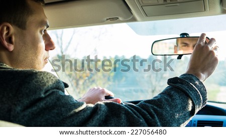 Experienced driver is looking in the rear view mirror in his car