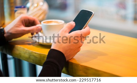 Man using a cell phone on cafe terrace and drink coffee