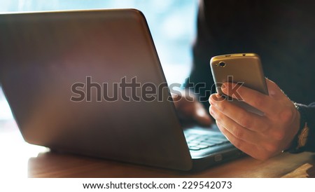 Man using a cell phone and laptop on cafe terrace