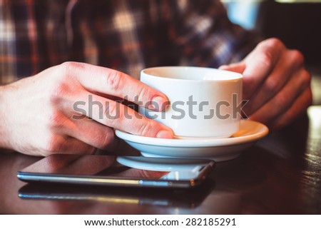 Man using a cell phone on cafe terrace and drink coffee. Male hands with cup and phone