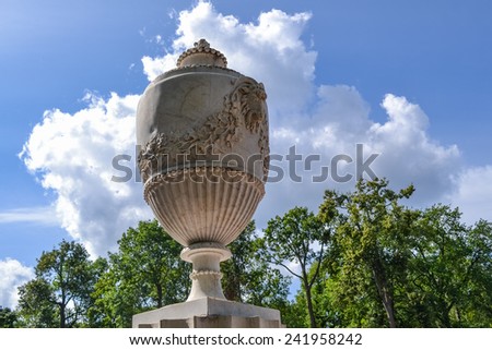 Beautiful decorative vase in the Park of Peterhof. White vase with floral ornaments on the background of trees and clouds. Antique vase, decoration of the Park.