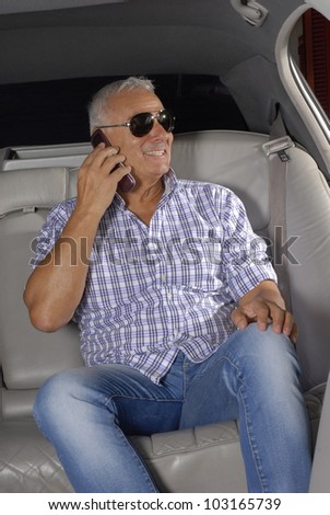 Senior rich man using a cell phone inside a car.