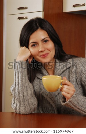 Beautiful young latin woman drinking a hot cup of drink in a kitchen,Drinking coffee.\
Woman cup.
