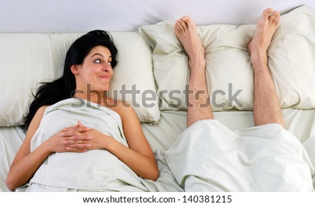 Barefoot man lying down on bed behind a woman.Couple resting on bed.