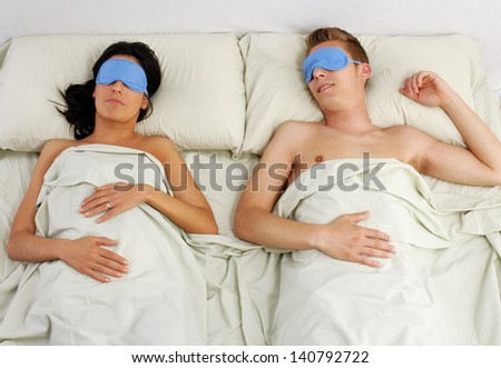 Sleeping couple in sleep eye mask on bed.