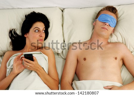 Young couple lying down on bed,cheating husband using a cell phone.