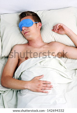 Sleeping young man in sleep eye mask on bed.