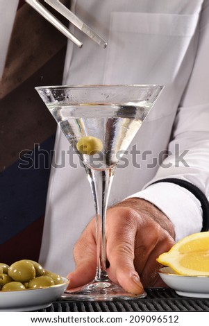 Bar man throwing olive on martini cocktail glass.Bartender preparing Martini cocktail.