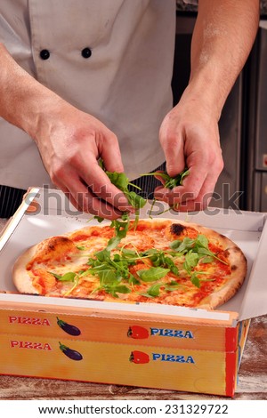 Cook adding ruccola on pizza ready to delivery. Preparing pizza delivery box.