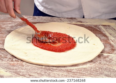 Cook adding tomato sauce on pizza dough. Cooking pizza.