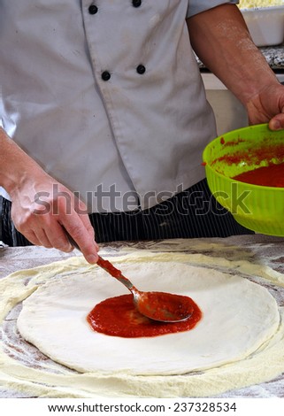 Cook adding tomato sauce on pizza dough. Cooking pizza.