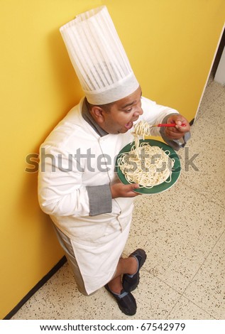 Hispanic chef eating pasta in a kitchen. Cook eating pasta in a kitchen.