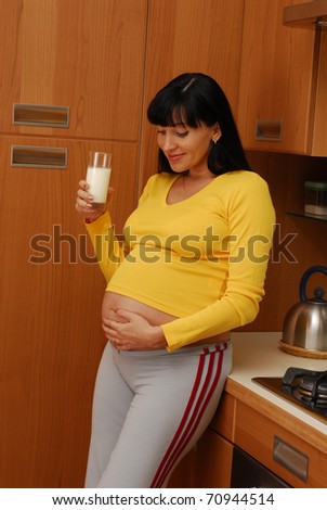 Young pregnant woman drinking milk in a kitchen.