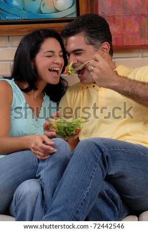Mid adult couple eating and sharing in a living room.