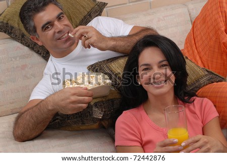 Couple watching tv and eating popcorn. Couple sharing in a living room.