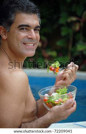 Young man eating vegetables behind a swimming pool.