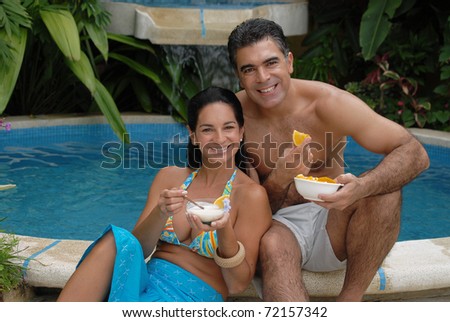 Young couple eating orange slices behind a swimming pool.