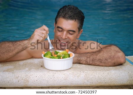 Young man eating vegetable salad in a swimming pool.