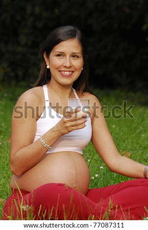 Beautiful pregnant woman drinking milk and relaxing in the park.