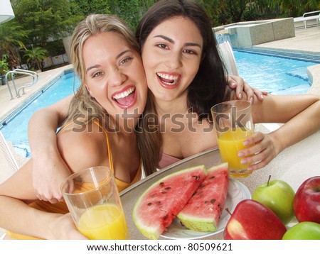 Young women enjoying and eating fruit behind a swimming pool.