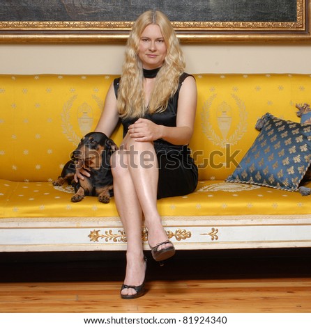 Young blonde woman with a little dog sitting on an elegant yellow sofa.
