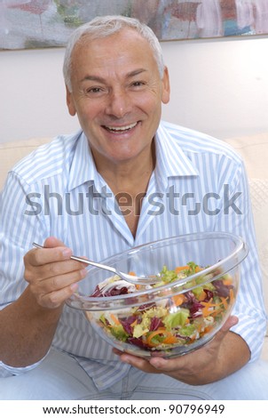 Happy senior man eating a fresh vegetable salad at home.