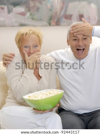 Expressive Senior couple eating popcorn and watching tv at home.
