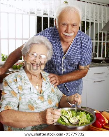 Happy senior couple preparing vegetable salad in the kitchen. Grandparents at kitchen preparing vegetable salad.