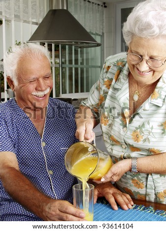 Grand parents drinking and pouring orange juice at kitchen.