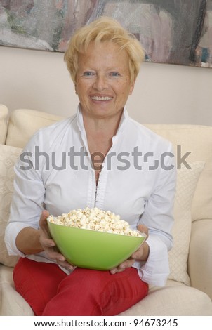 Mature woman enjoying in a living room eating popcorn.