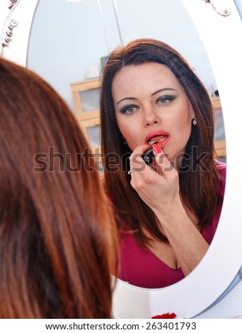 Woman applying red lipstick in dressing room mirror