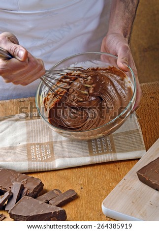 Cook mixing dark chocolate cream on glass bold. Preparing chocolate recipe.