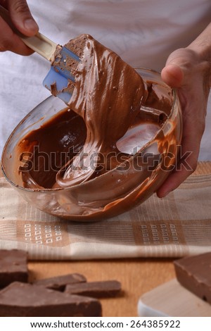 Cook mixing dark chocolate cream on glass bold. Preparing chocolate recipe.