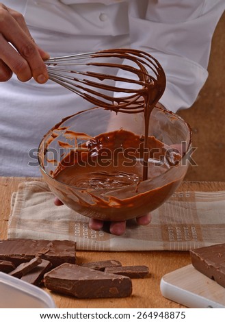 Cook mixing and tasting dark chocolate cream on glass bold. Preparing chocolate recipe.