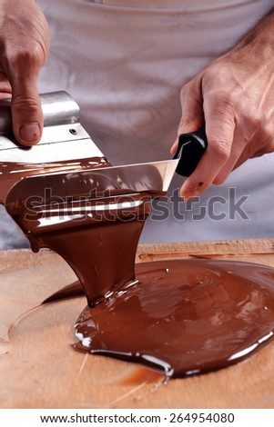 Cook mixing chocolate cream with professional chocolate spatula. Melted dark chocolate.