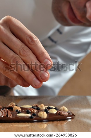 Cook preparing nuts dark chocolate bar.Adding nuts fruits on dark chocolate bar.
