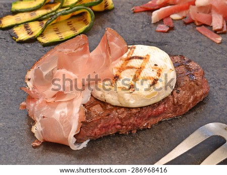 Grilled beef steak and ham with cheese on stone and vegetables.