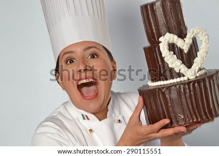 Happy pastry cook woman holding a big chocolate cake. Cake design woman.