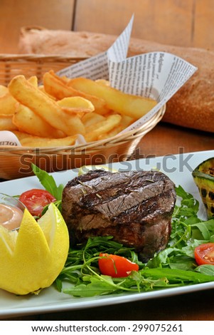 Medium grilled beef steak on salad dish and potatoes fries.