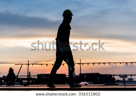 Construction site, silhouettes of workers on scaffolding with blue sky background or twilight time