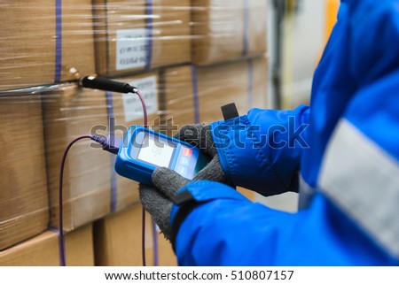 Hand of worker using thermometer to temperature measurement in the goods boxes with ready meals after import in the cold room or warehouse for keep temperature room.