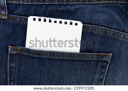 Part of white notebook papaer in the back pocket of blue denim jeans