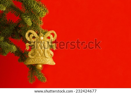 Gold Christmas bell ornament hanging on Christmas tree branch on a bright red background