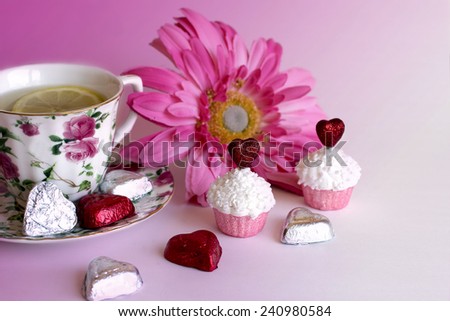 Valentine background with pink flower and chocolate heart candy; Valentine cupcakes Tea time; Tea cup with pink flower two cupcakes and heart candy on pink background