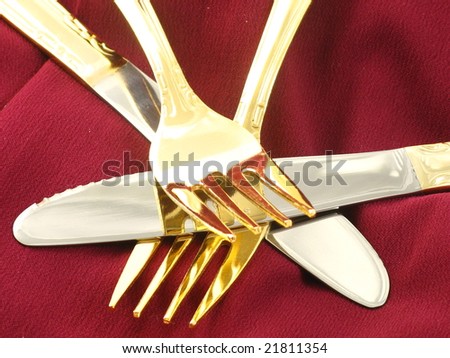 Abstract Shiny Gold Forks and Knives Arranged and Isolated on a Dark Red Burgundy Background as a Closeup