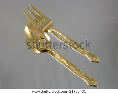 Shiny Gold Dining Serving Spoon and Fork Arranged and Isolated on a Reflective Silver Background as an Abstract Closeup