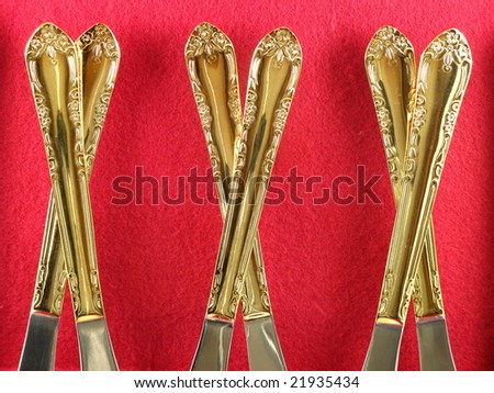 Shiny Gold Dining Flatware Knives Arranged and Isolated on a Dark Red Burgundy Background as an Abstract Closeup