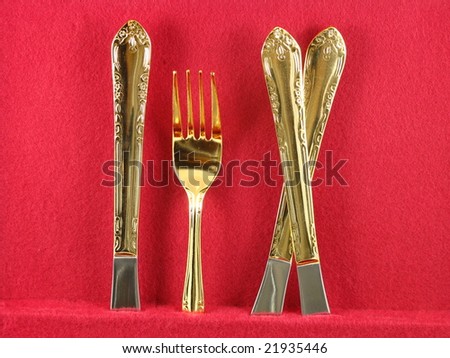 Shiny Gold Dinnerware Fork and Knives Arranged and Isolated on a Dark Red Burgundy Background as an Abstract Closeup