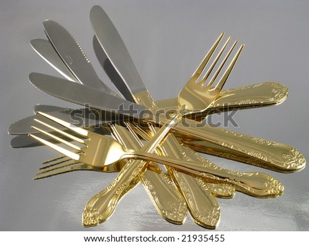 Shiny Gold Flatware Forks and Knives Arranged and Isolated on a Reflective Silver Background as an Abstract Closeup