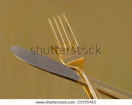 Shiny Gold Dinnerware Fork and Knife Arranged and Isolated on a Reflective Gold Background as an Abstract Closeup
